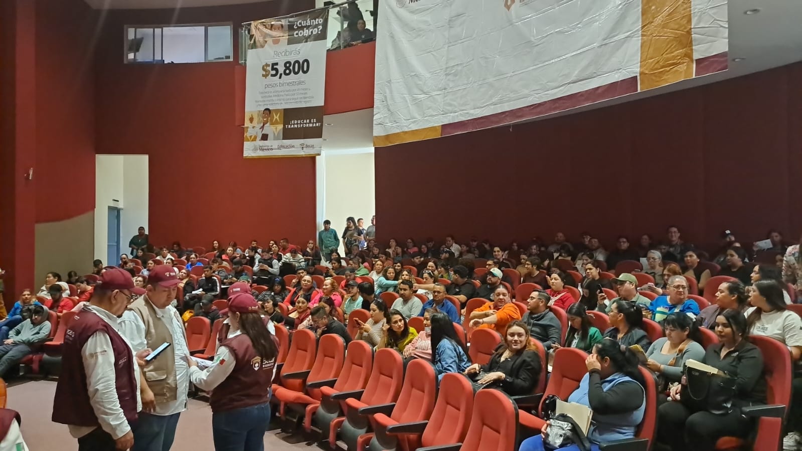 Personas sentadas en butacas en un auditorio y otras personas mayores
