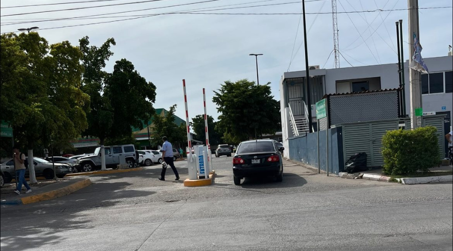 Entrada a estacionamiento de plaza comercial en Los Mochis, donde se ve la pluma levantada para otorgarle el acceso a un automóvil y un guardia de seguridad revisando la zona