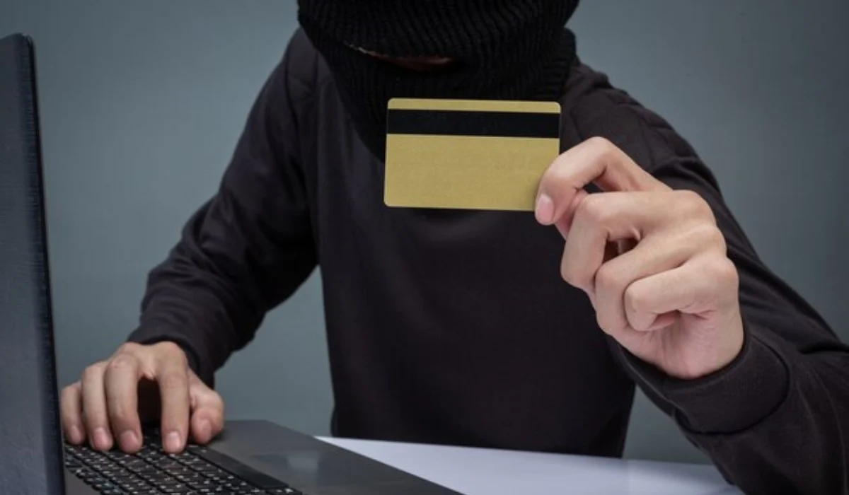 Sujeto sospechoso sosteniendo una tarjeta y tocando una computadora.