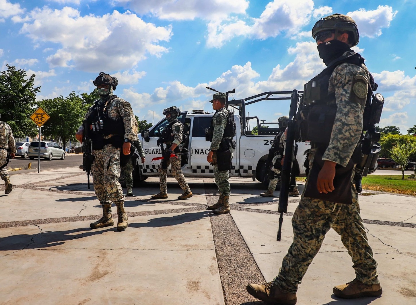 Elementos de la guardia nacional uniformados, encapuchados y armados debajo de su vehículo realizando un operativo