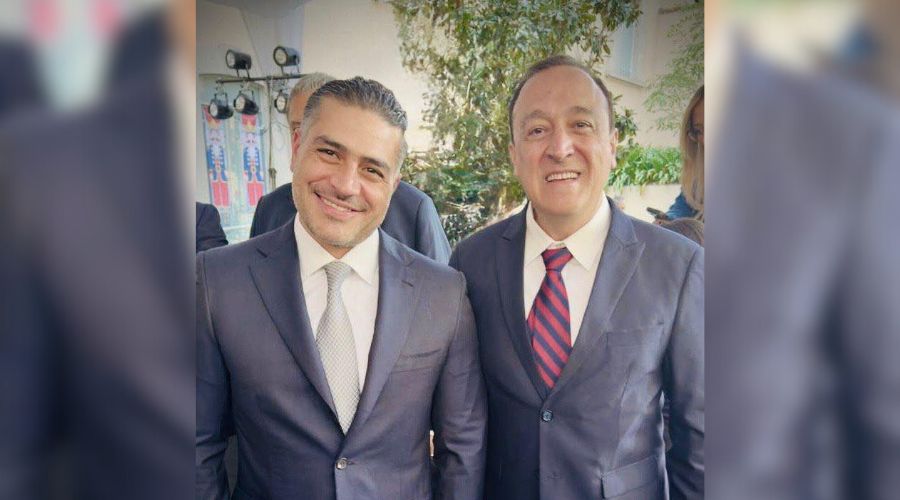 Dos hombres de traje sonriendo y viendo hacia el frente
