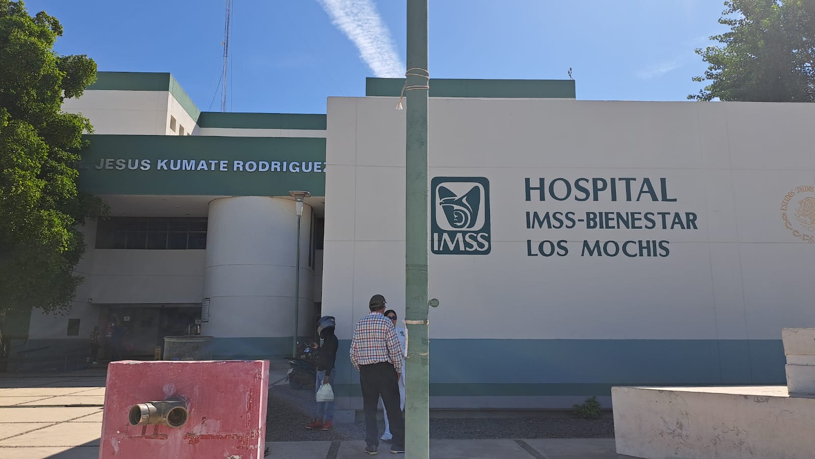Fachada de un hospital en tonos verde y blanco, con personas afuera