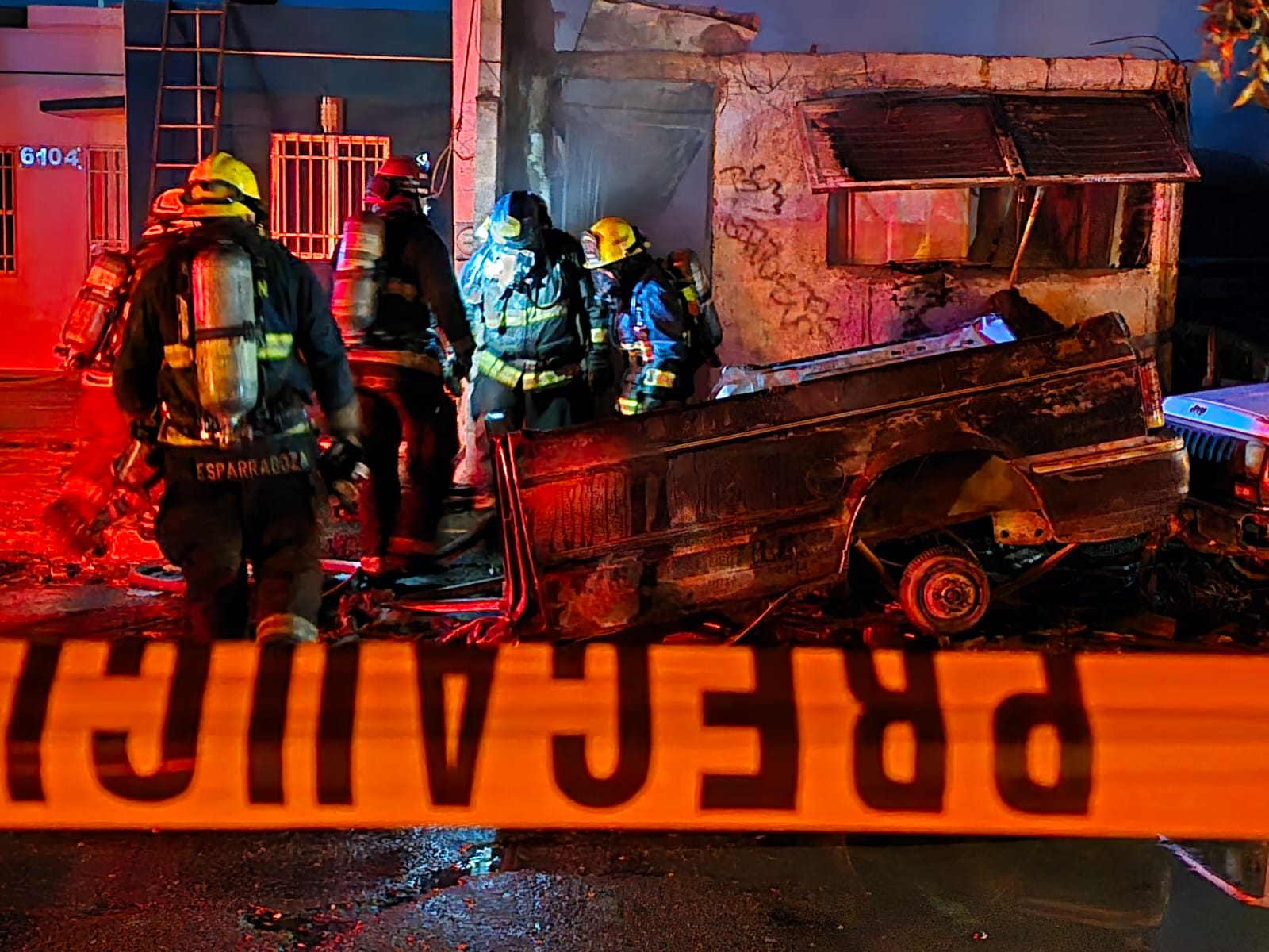 Cinta amarilla de precaución, al fondo se observan elementos de bomberos en un lugar donde sale humo por un incendio