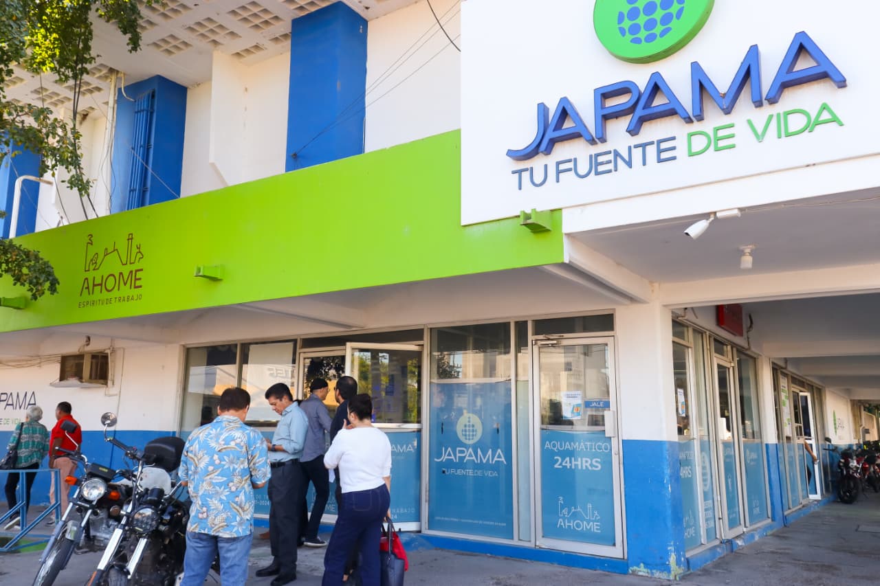 PErsonas paradas en la banqueta afuera de un edificio en colores azul, verde y blanco