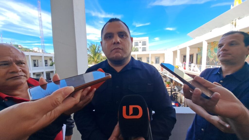 PErsona viendo hacia el frente con micrófonos y celulares apuntando hacia la cara de la persona