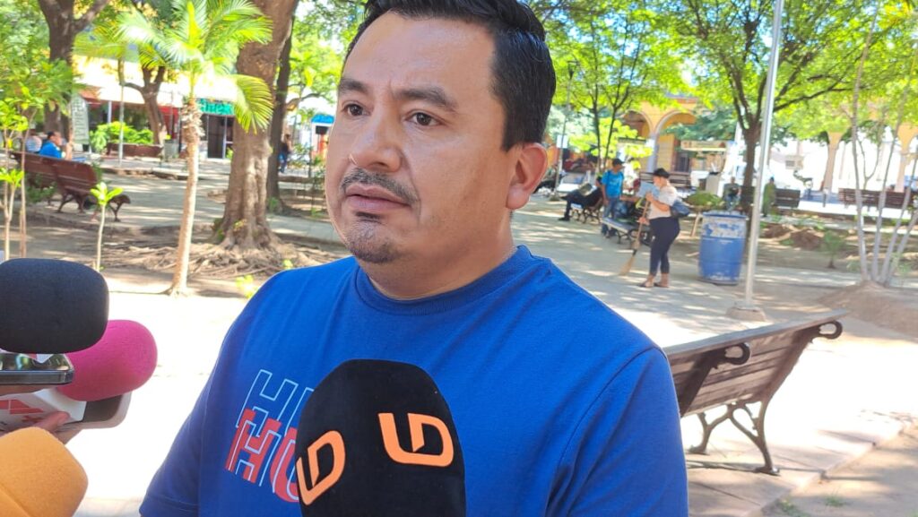 Persona con playera azul hablando a micrófonos