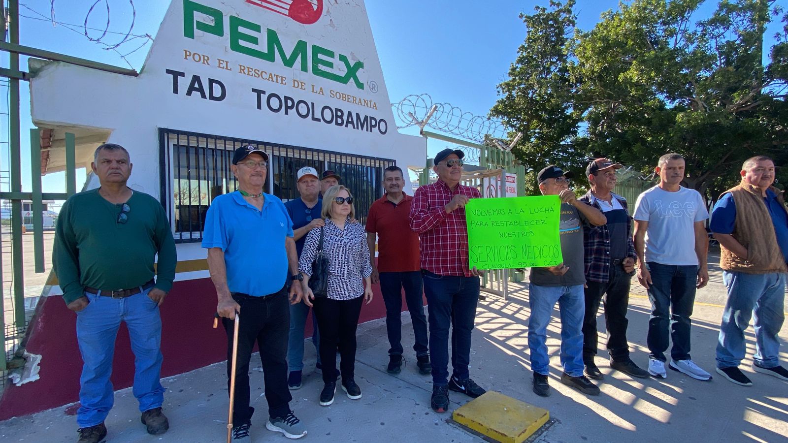Personas manifestándose con una cartulina afuera de un letrero de Pemex