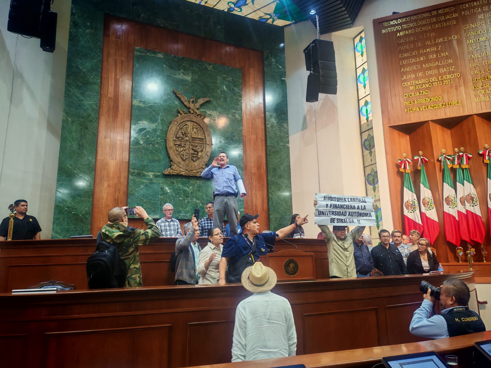 Personas dentro de la sala del Congreso del Estado con lonas de protesta