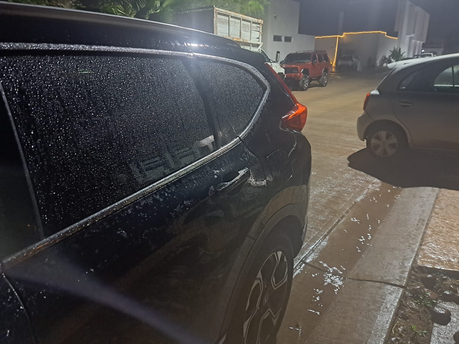 Carro color negro mojado y pequeños charcos en la calle por la lluvia