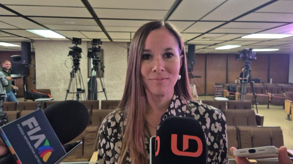 Mujer de pelolargo viendo al frente sonriendo y un micrófono negro con las letras LD en color naranja
