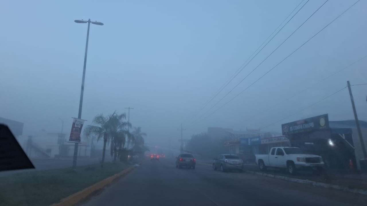Calle con carros y negocios que se van perdiendo entre la densa capa de neblina