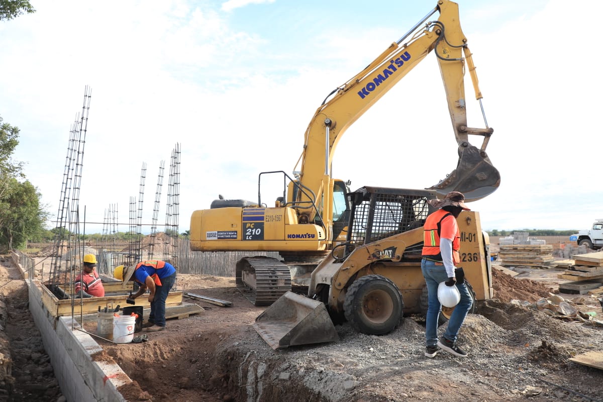 Maquina retroexcavadora en un una construcción, con personas trabajando en una obra