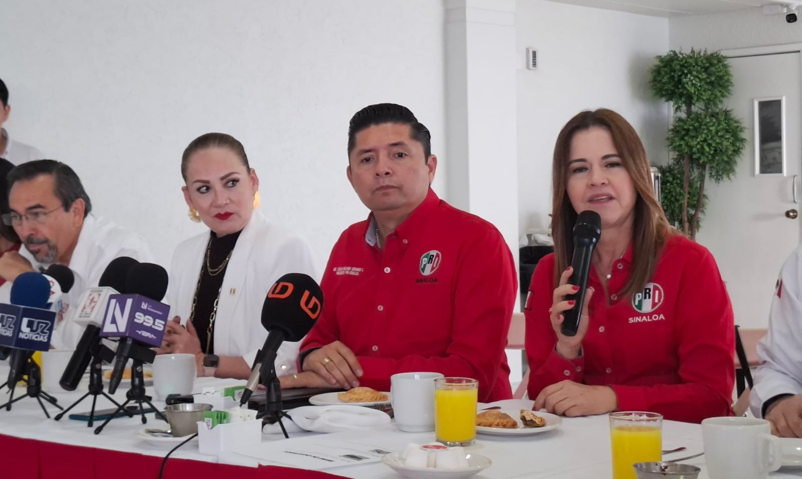 Personas sentadas atrás de una mesa con micrófonos frente a ellos en una rueda de prensa