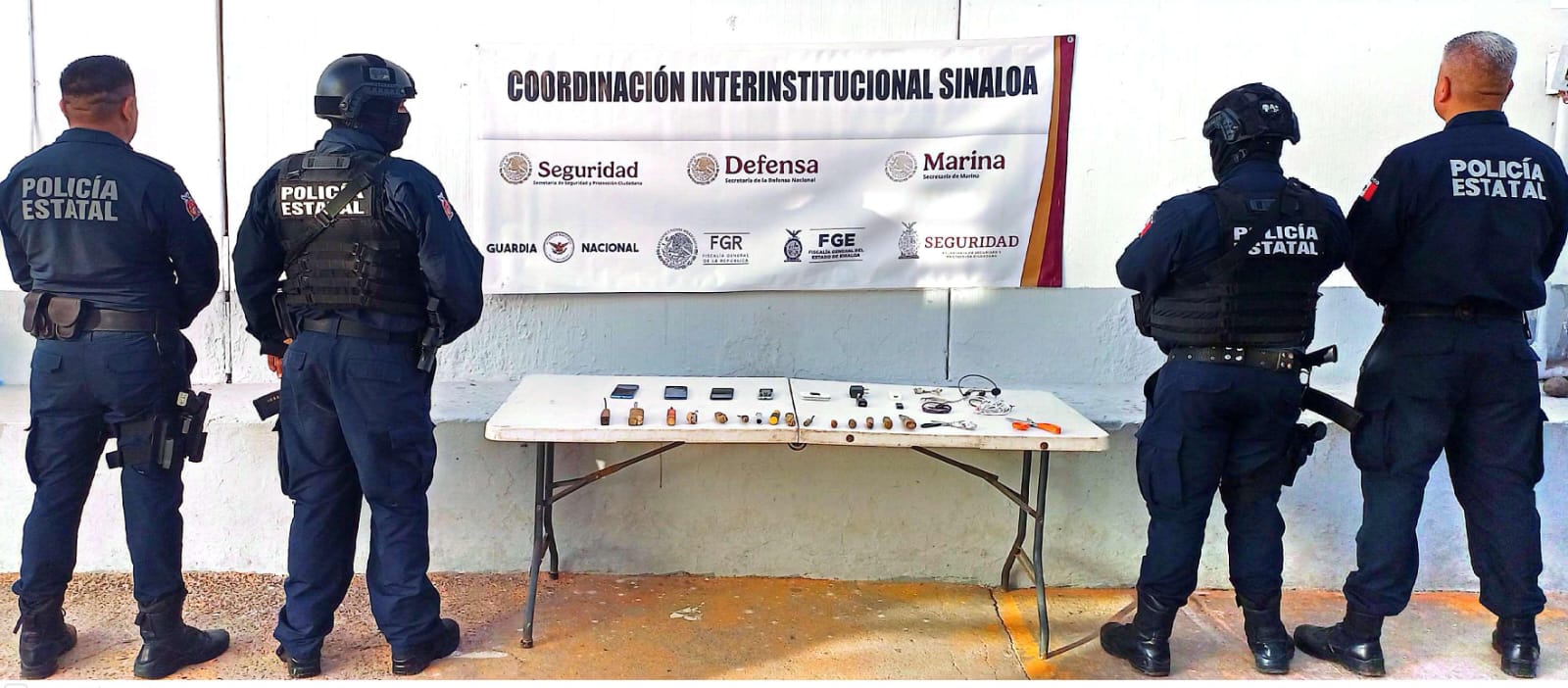 Policías junto a una lona de Seguridad y objetos asegurados en una mesa