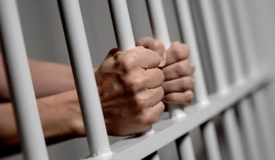 Persona sujeta rejas de una celda en prisión