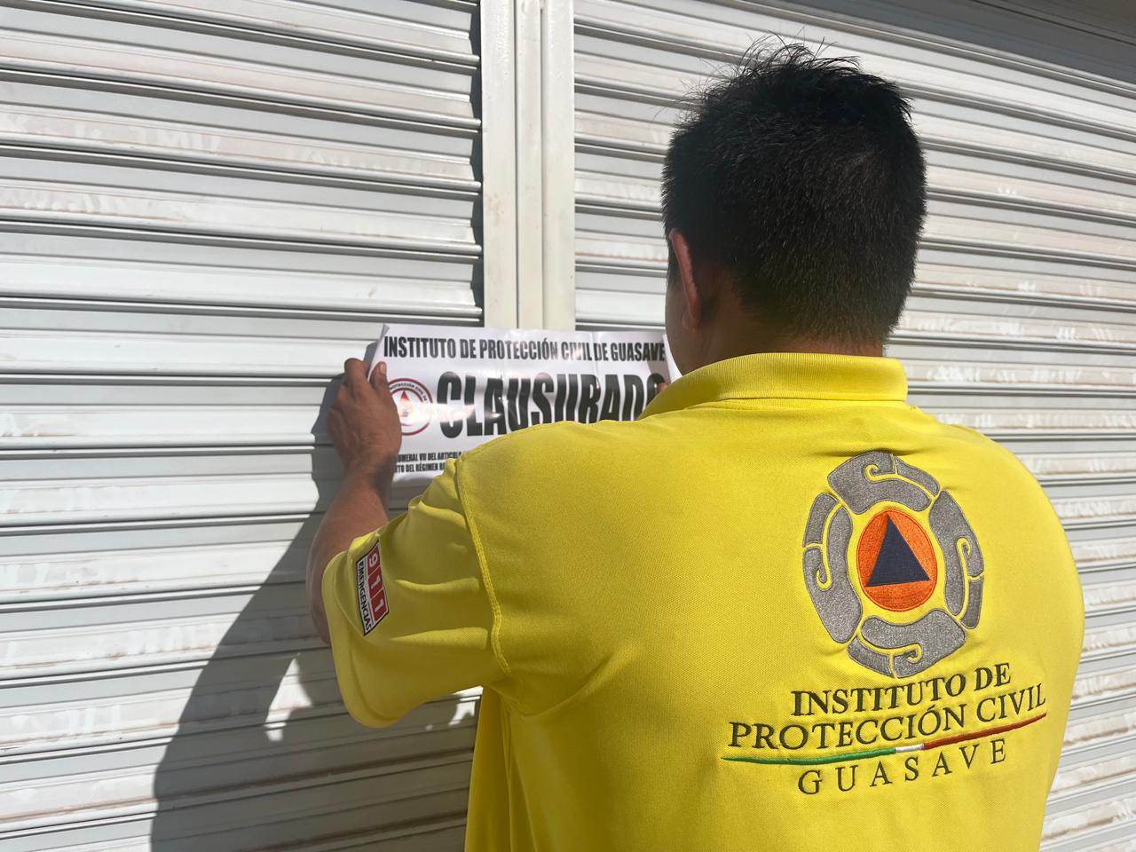 PErsonal de Protección Civil colocando una hoja con la leyenda de clausurado en la cortina de un establecimiento