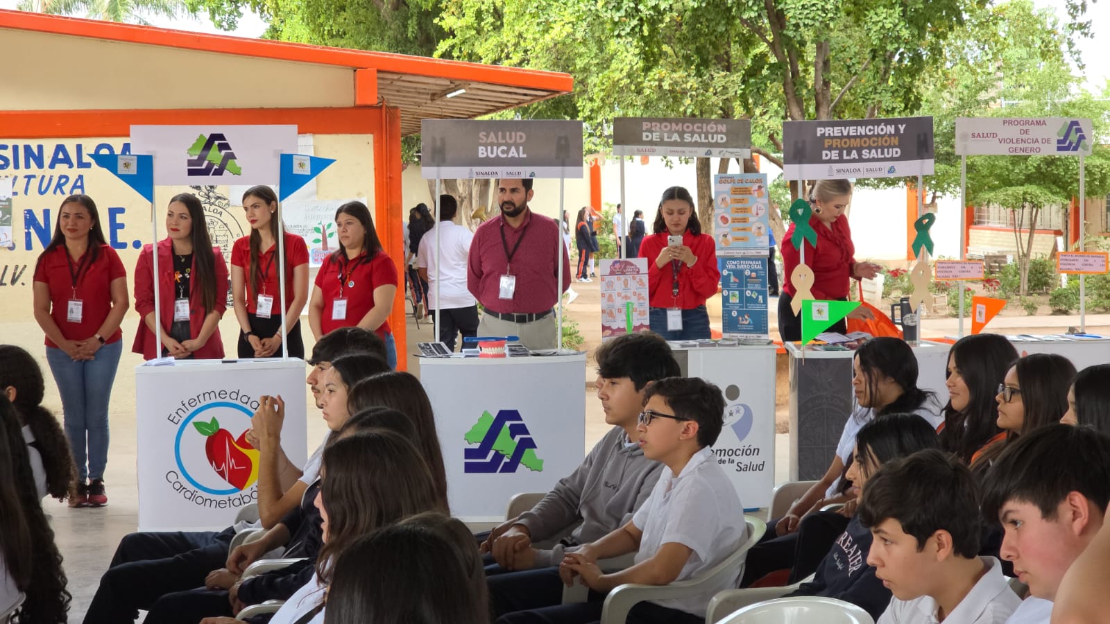 Personas en estantes promoviendo jornada de salud y al frente jóvenes sentados
