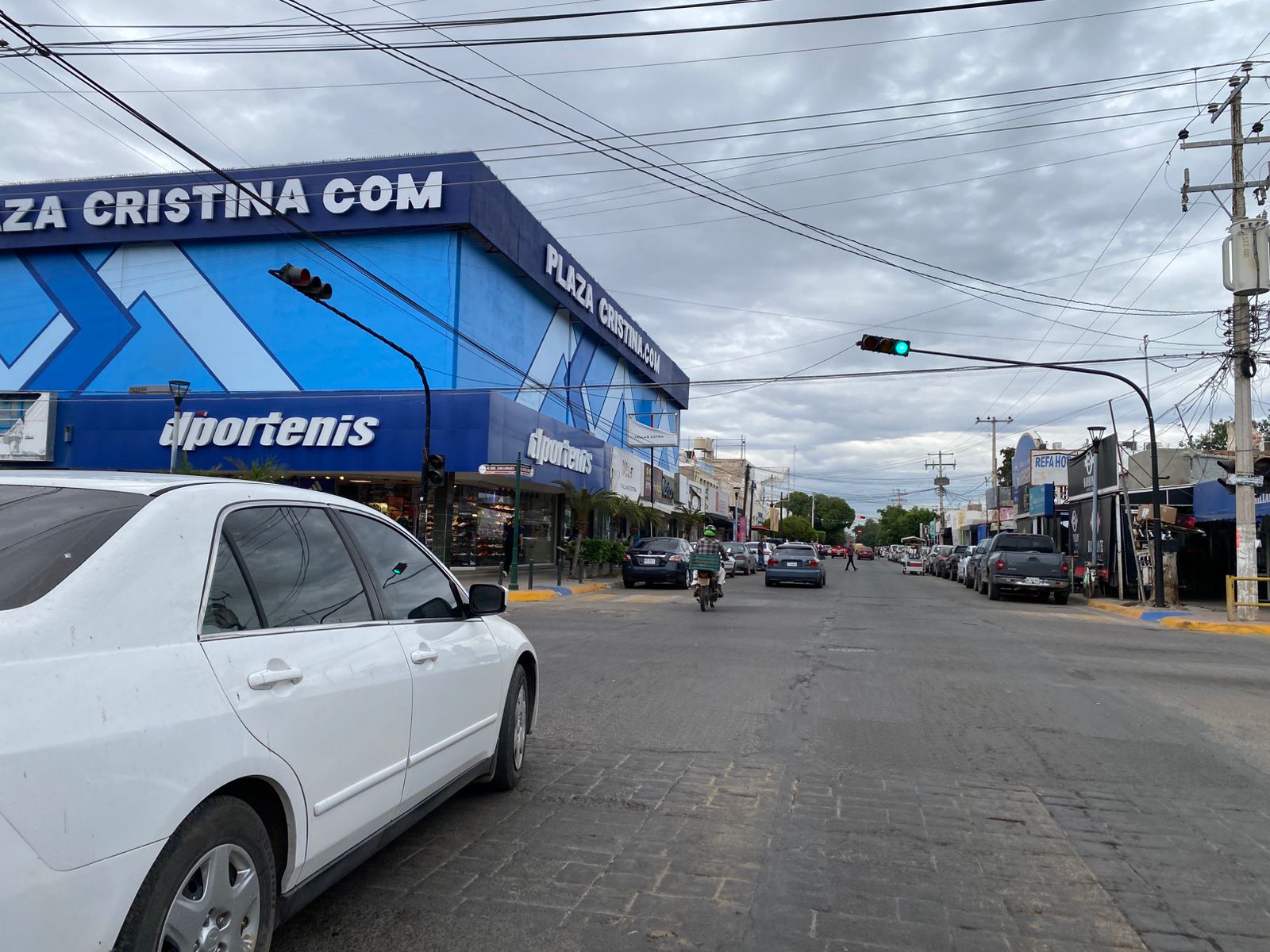 Calle transitada de Guasave, donde se ve un semáforo en verde y carros y personas atravesando la calle