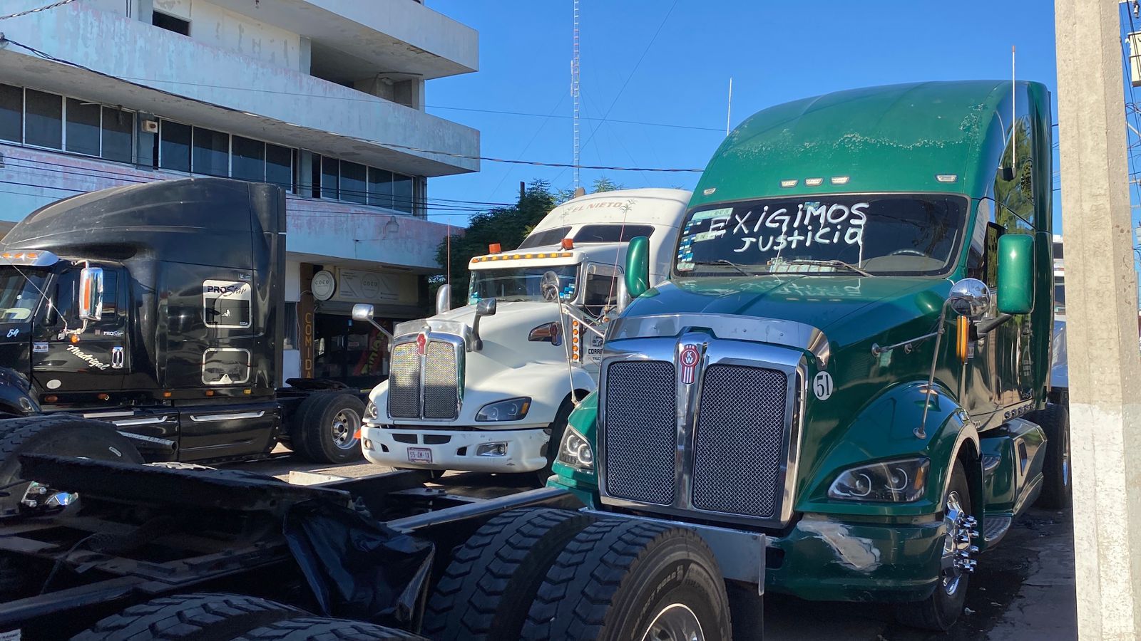Tráileres formados en fila tapando la calle, uno de ellos con una leyenda escrita en el parabrisas en manera de protesta