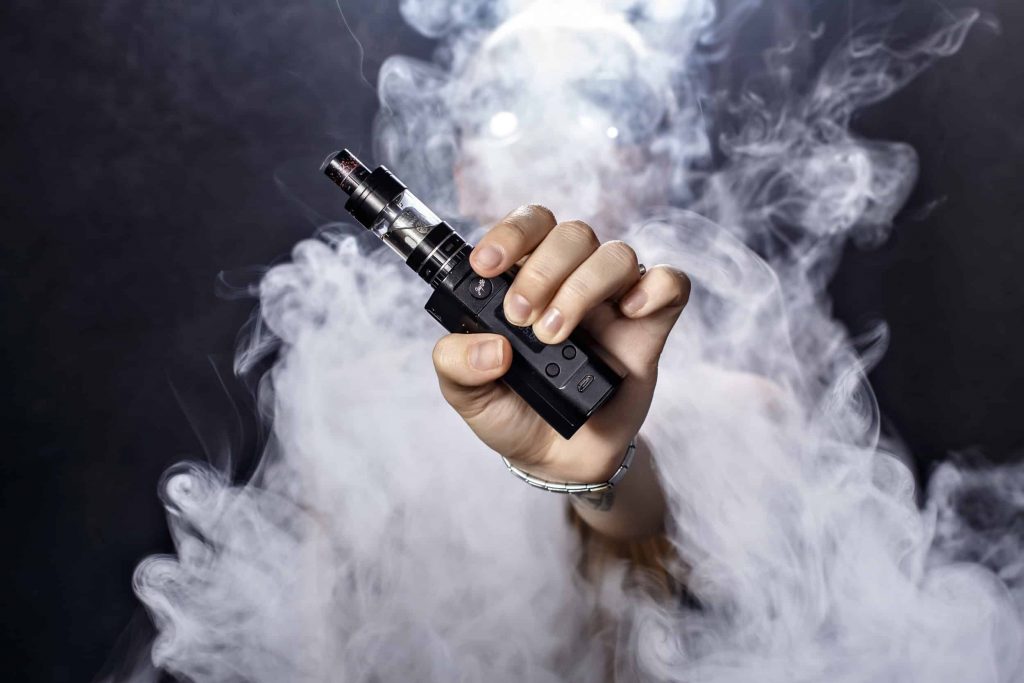 Mano sosteniendo un vapeador entre una nube de humo.