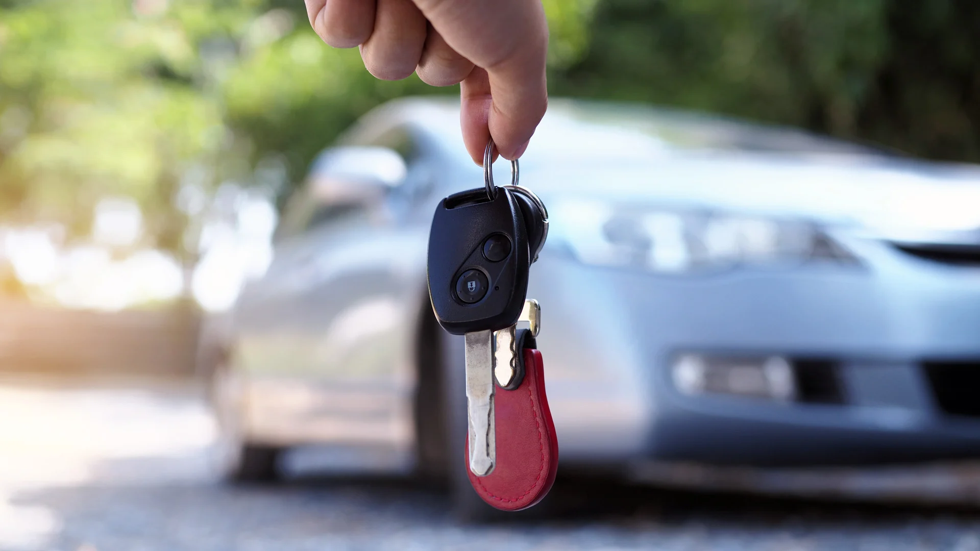 Mano sosteniendo unas llaves y al fondo un carro