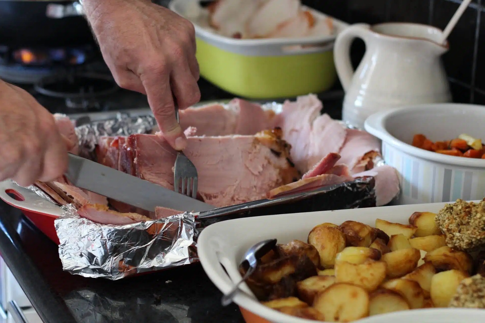Platillos de comida y una persona partiendo con cuchillo y tenedor un pedazo de jamón