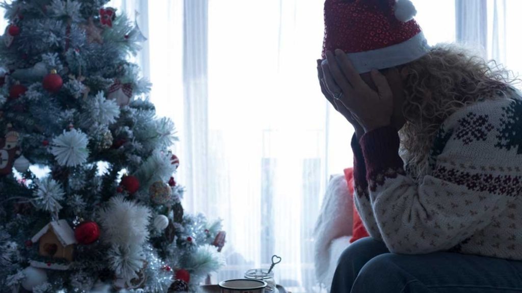 Mujer con las manos en la cara junto a árbol de navidad