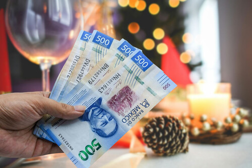 Cuatro billetes de 500 en una mano con fondo navideño