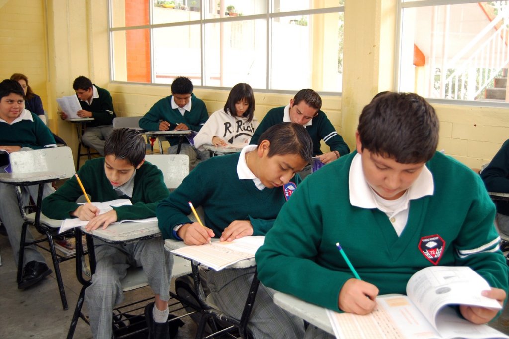Alumnos sentados realizando trabajados en butacas en un salón de clases