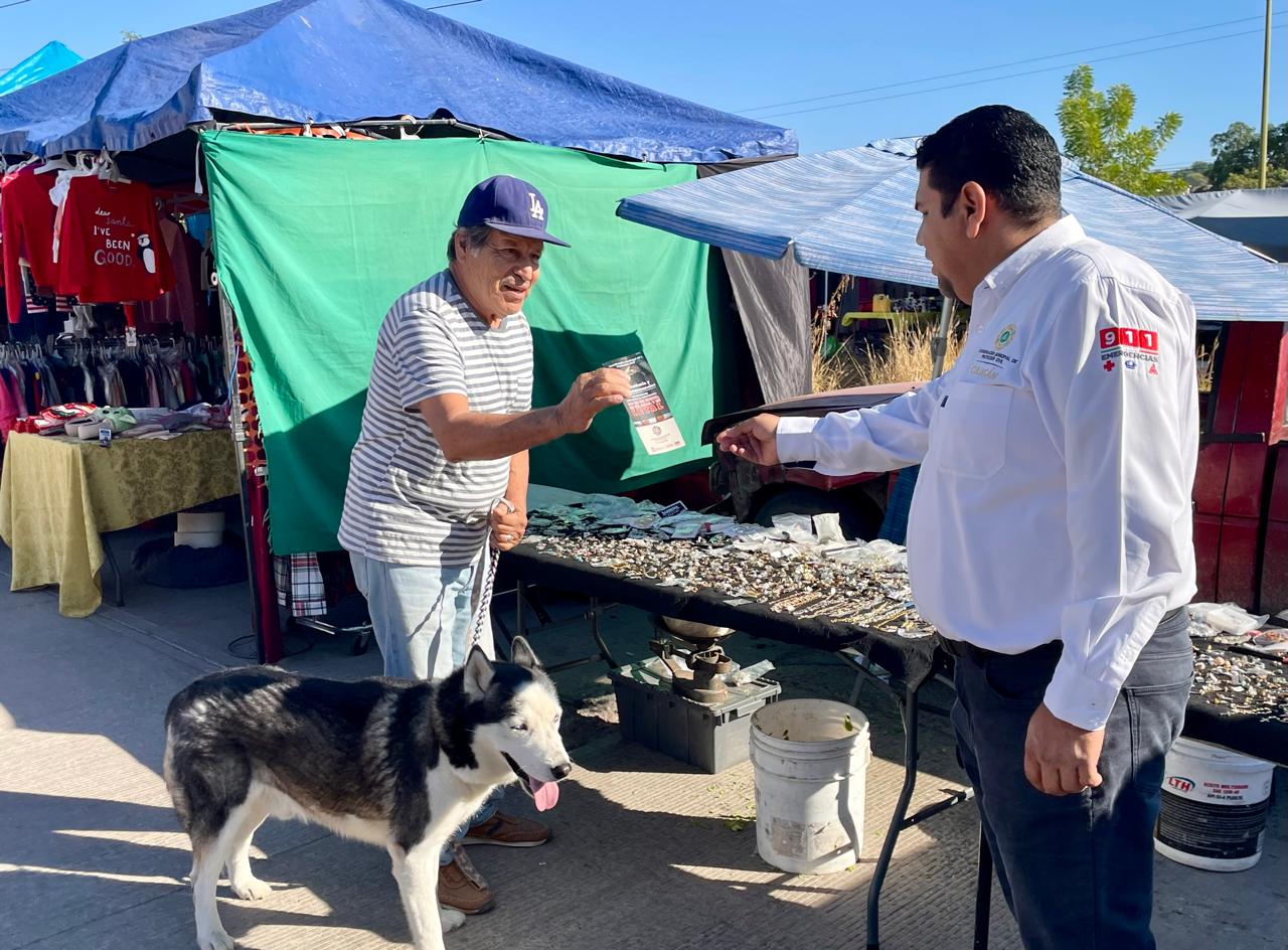Persona entregando un folleto a otra persona y atrás hay una mesa con productos y un perro en el piso