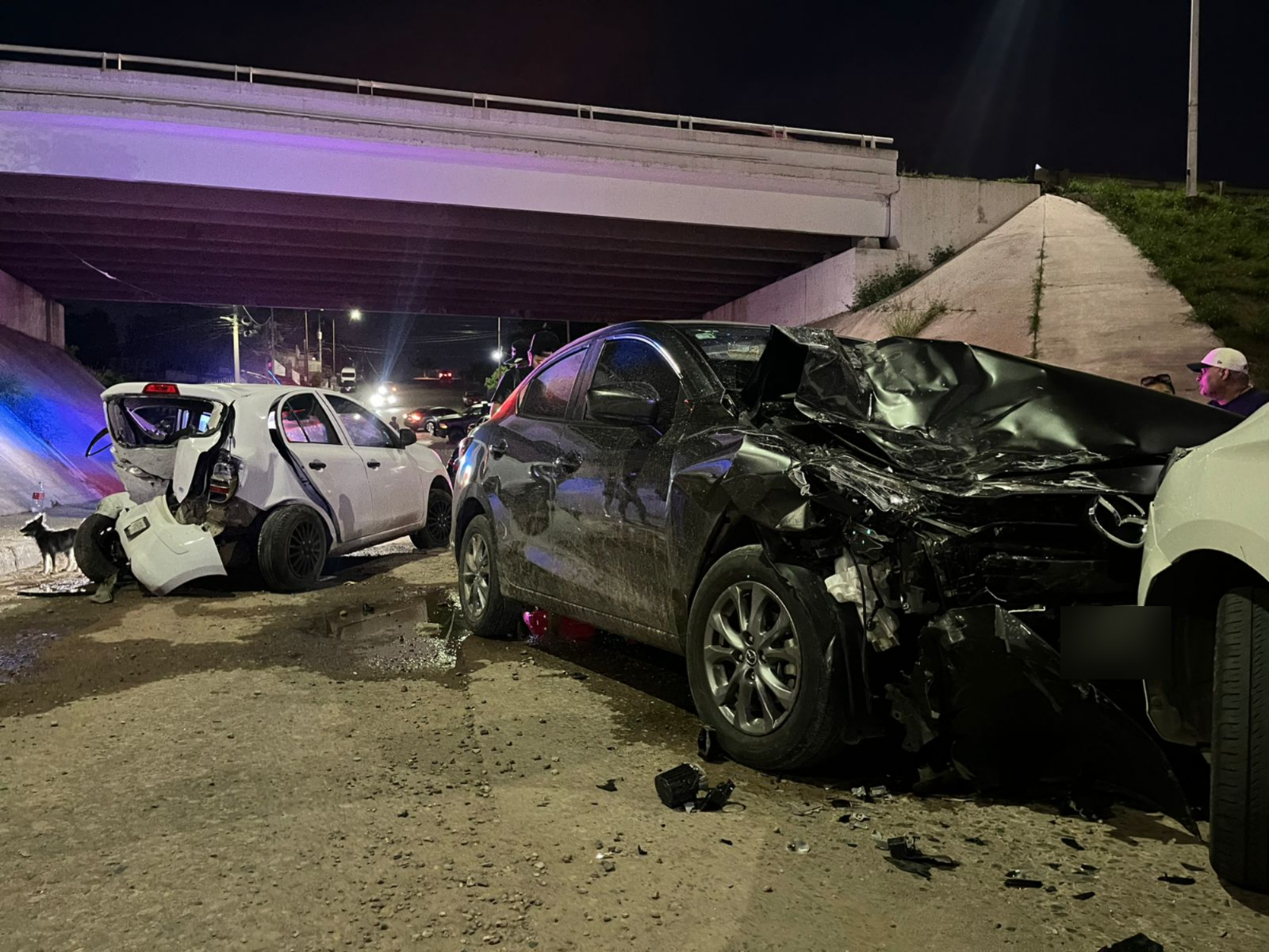 Un carro negro en primer pplano impactado por l aparte delantera, mientras que otro carro al fondo de color blanco chocado de la parte trasera