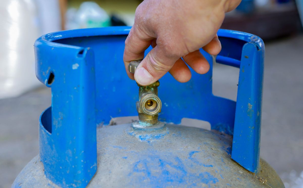 Mano agarrando la boquilla de un tanque de gas color azul que tiene tierra