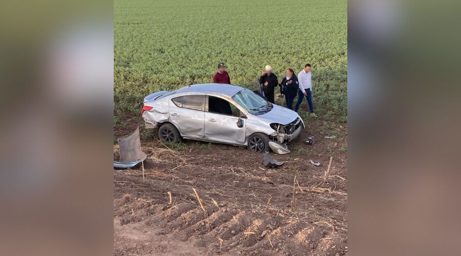 Auto con golpes por accidente vial y personas alrededor en un lugar tipo sembradío