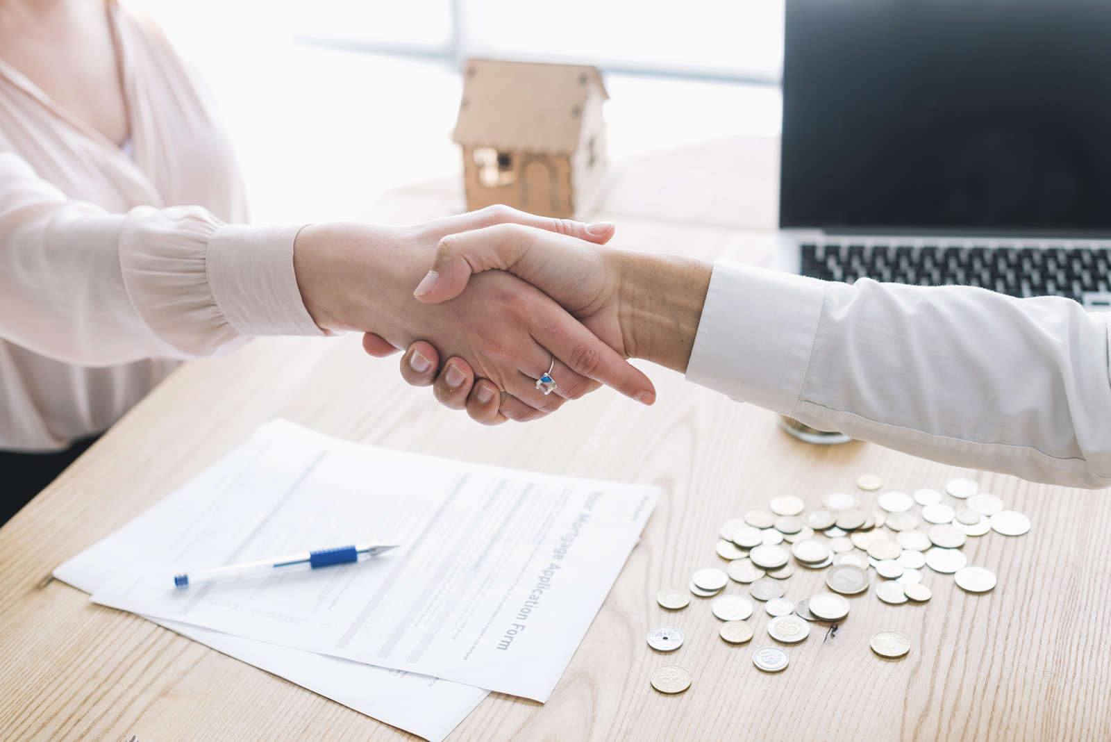 Dos personas dándose la mano y debajo un escritorio con hojas y monedas sobre el