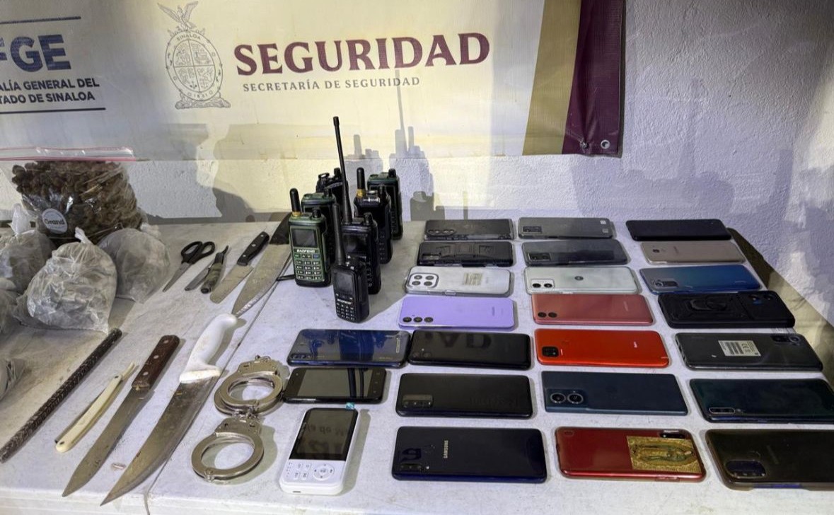 Mesa con celulares y objetos y al fondo una lona con la leyenda "Seguridad"