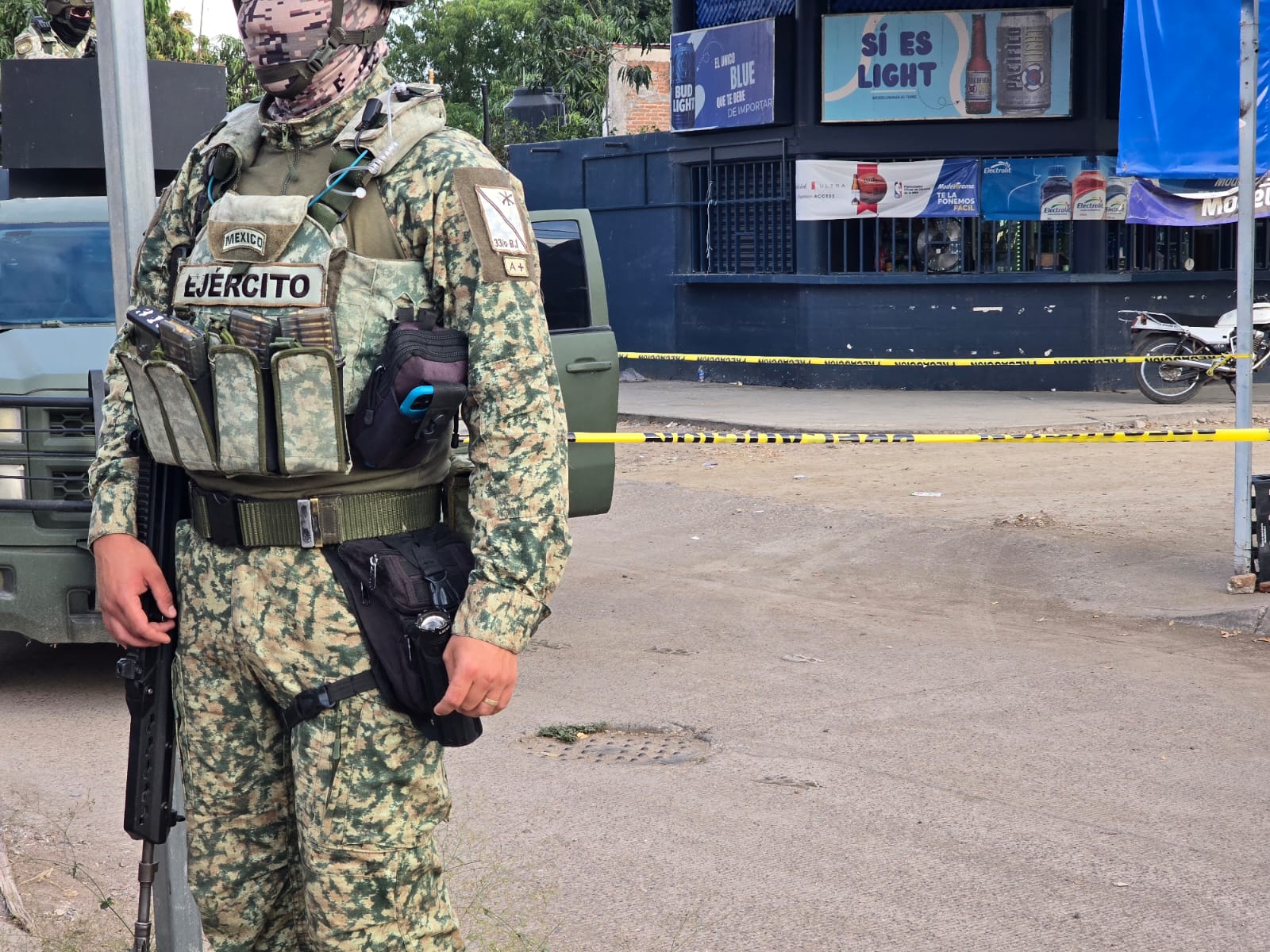 Militar de frente y al fondo un expendio cervecero con una cinta amarilla