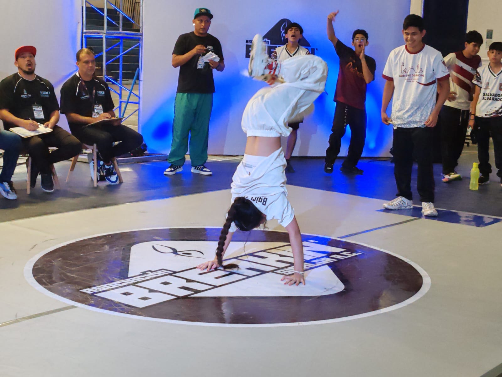 Atleta de breaking parado de manos en medio del escenario