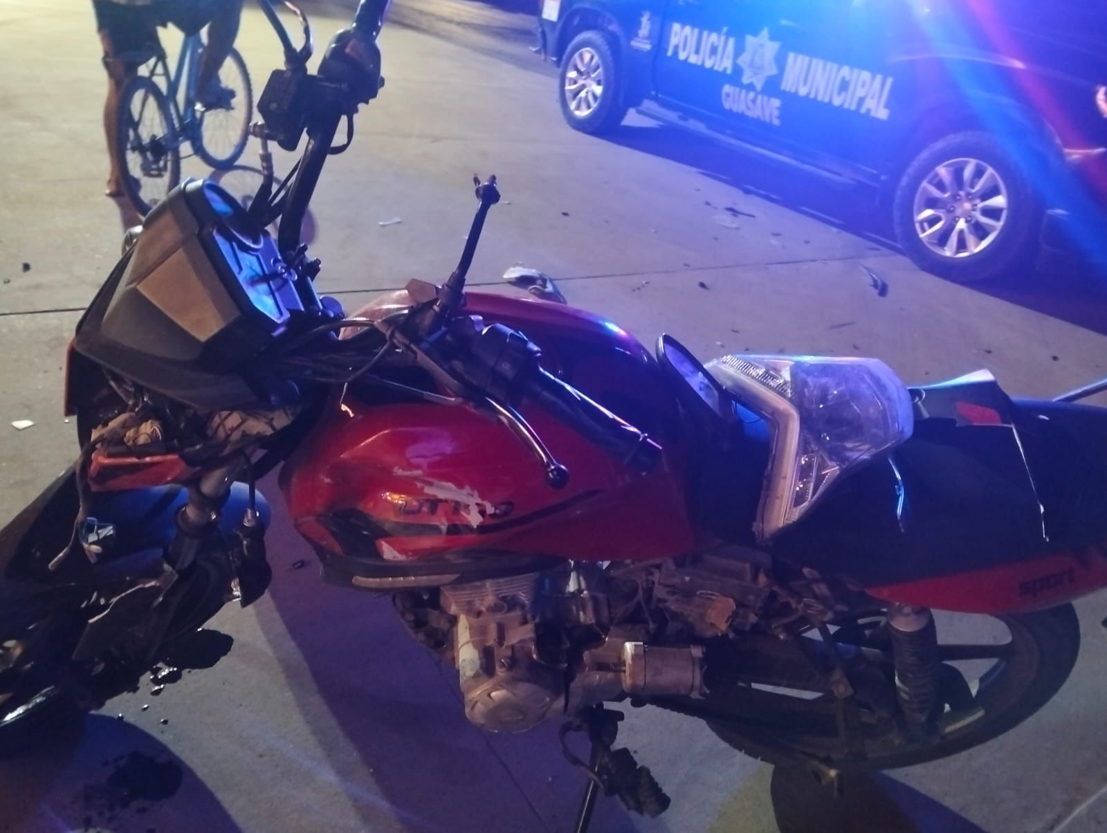 Motocicleta en una calle y al fondo una unidad policiaca con destellos de luz azul