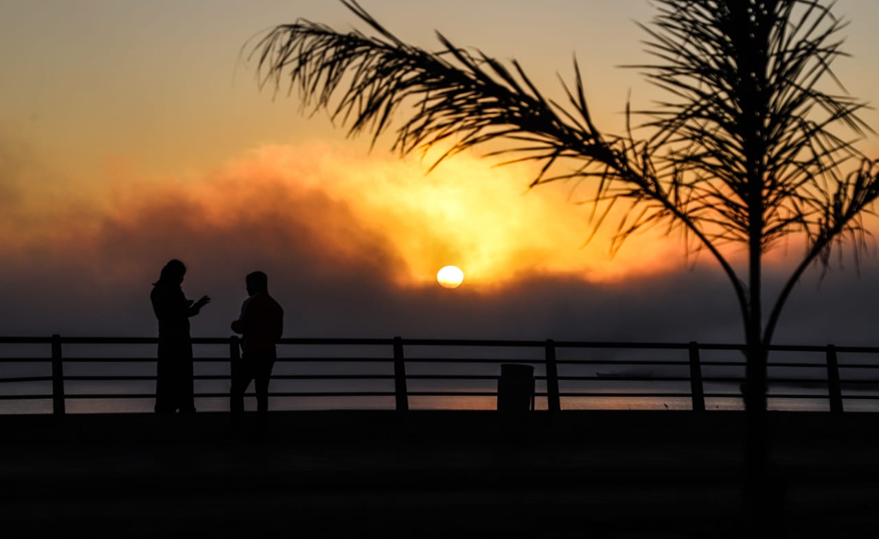 Puesta de sol en una playa, dos personas en un puente y una palmera