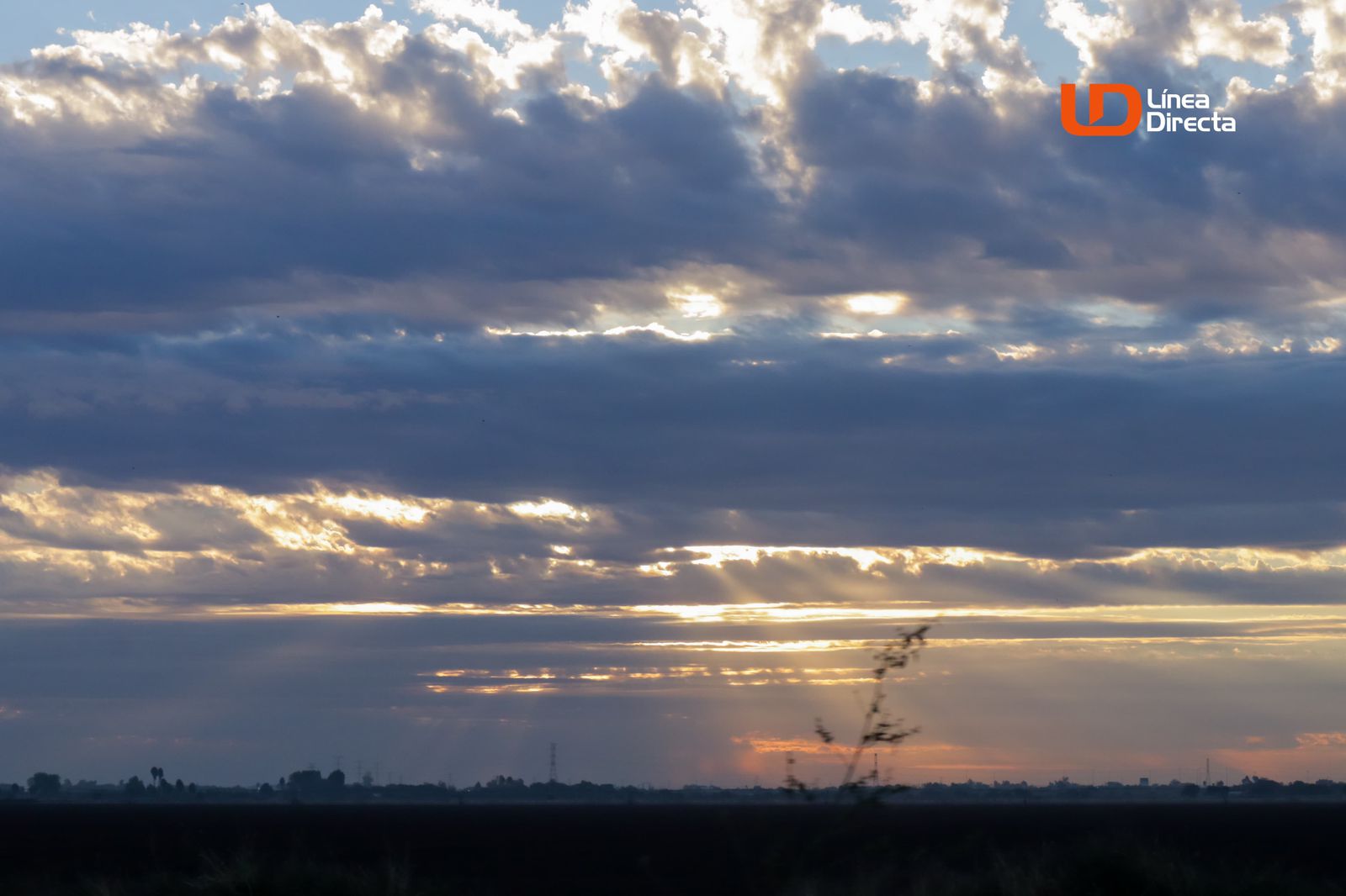 Cielo medio nublado con destellos de la luz del sol entre las nubes en un campo