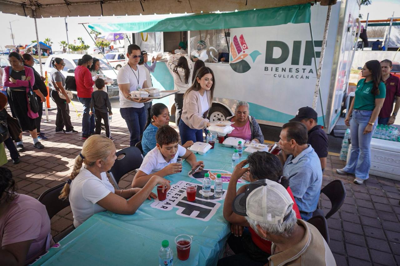Personas sentadas en una mesa y autoridades de DIF Culiacán repartiendo comida