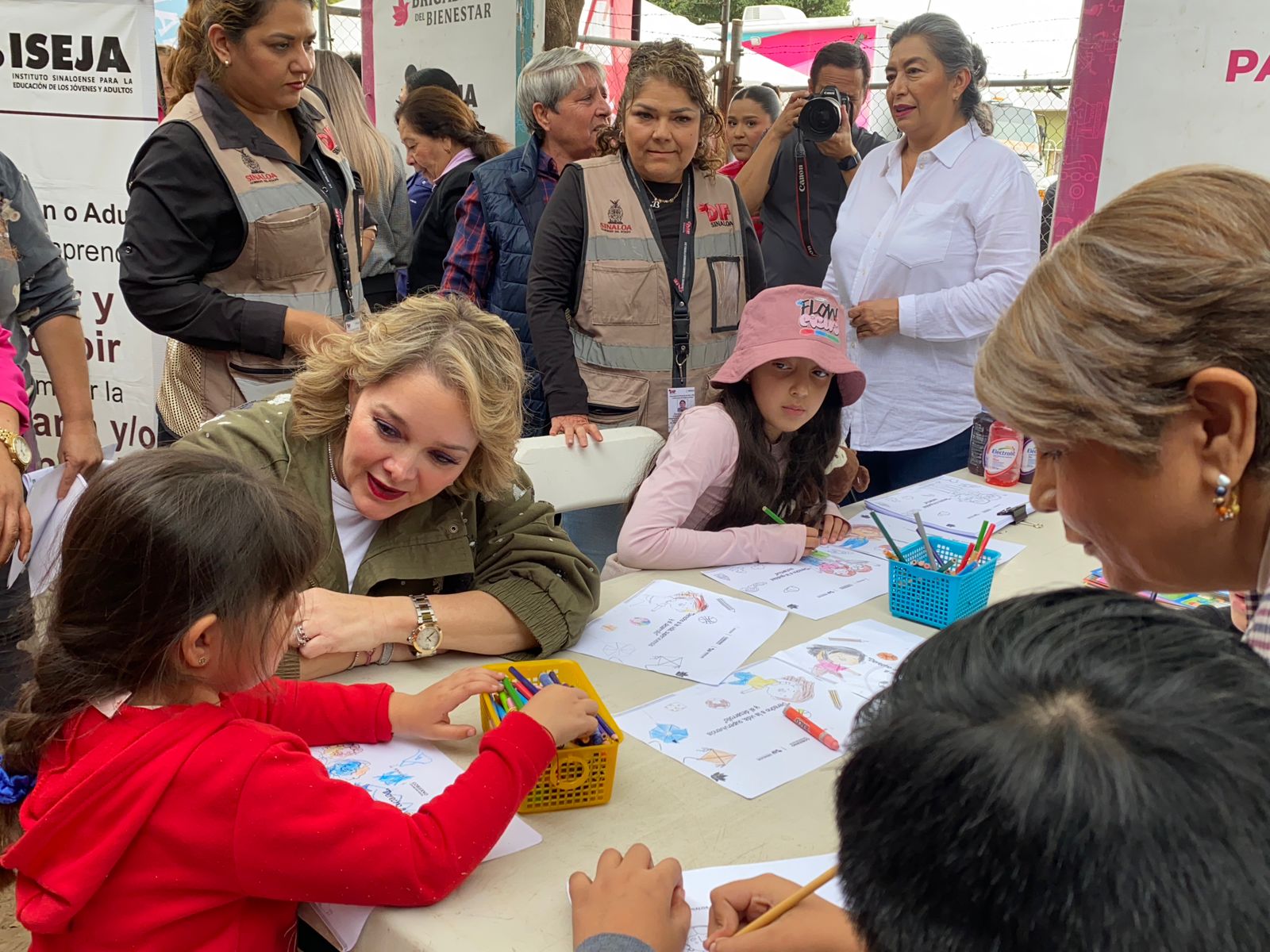 Niños sentados en una mesa coloreando y autoridades de Guasave platicando con ellos