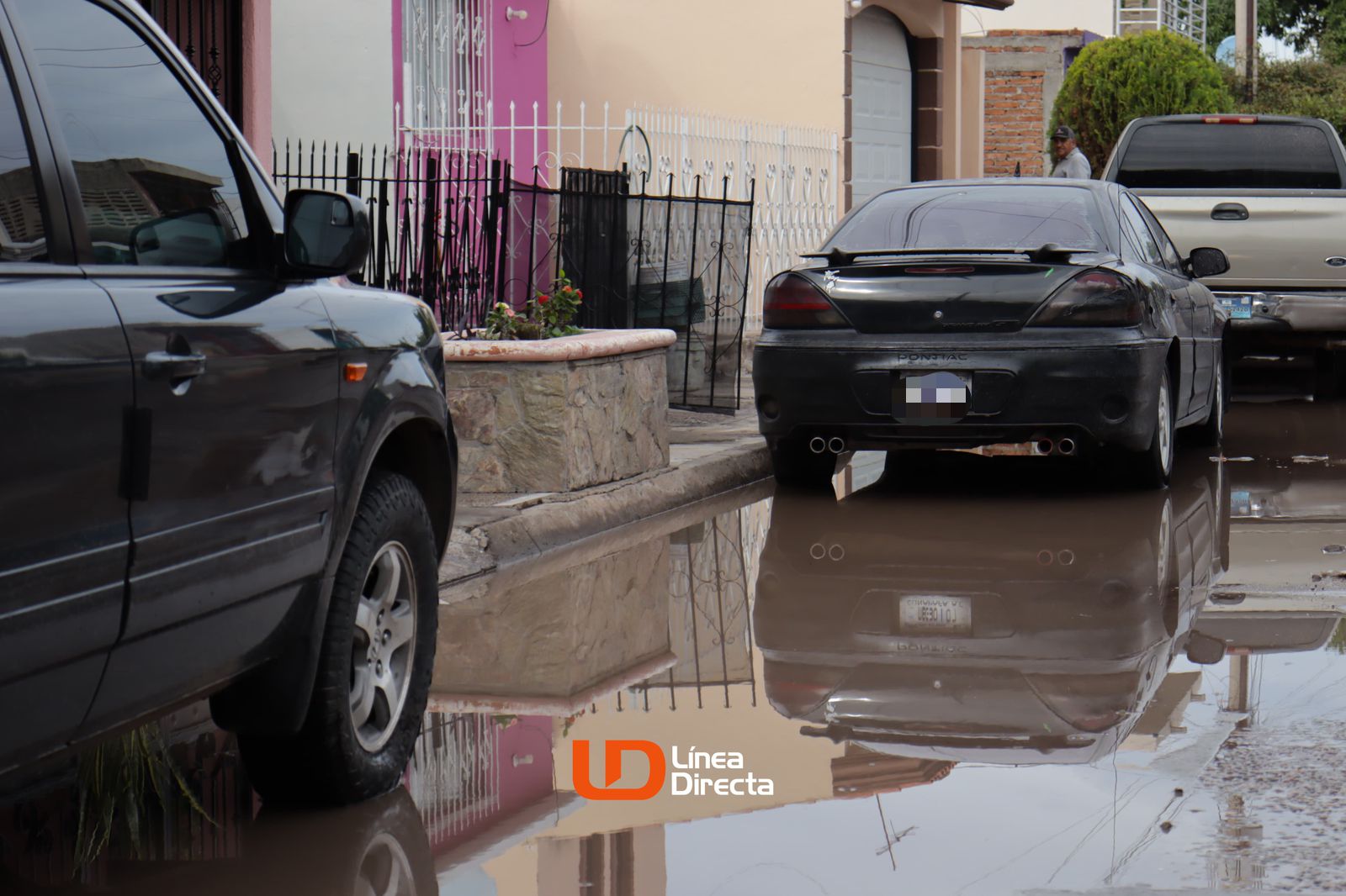 Carros estacionados en una calle con un charco de aguas negras por el drenaje colapsado