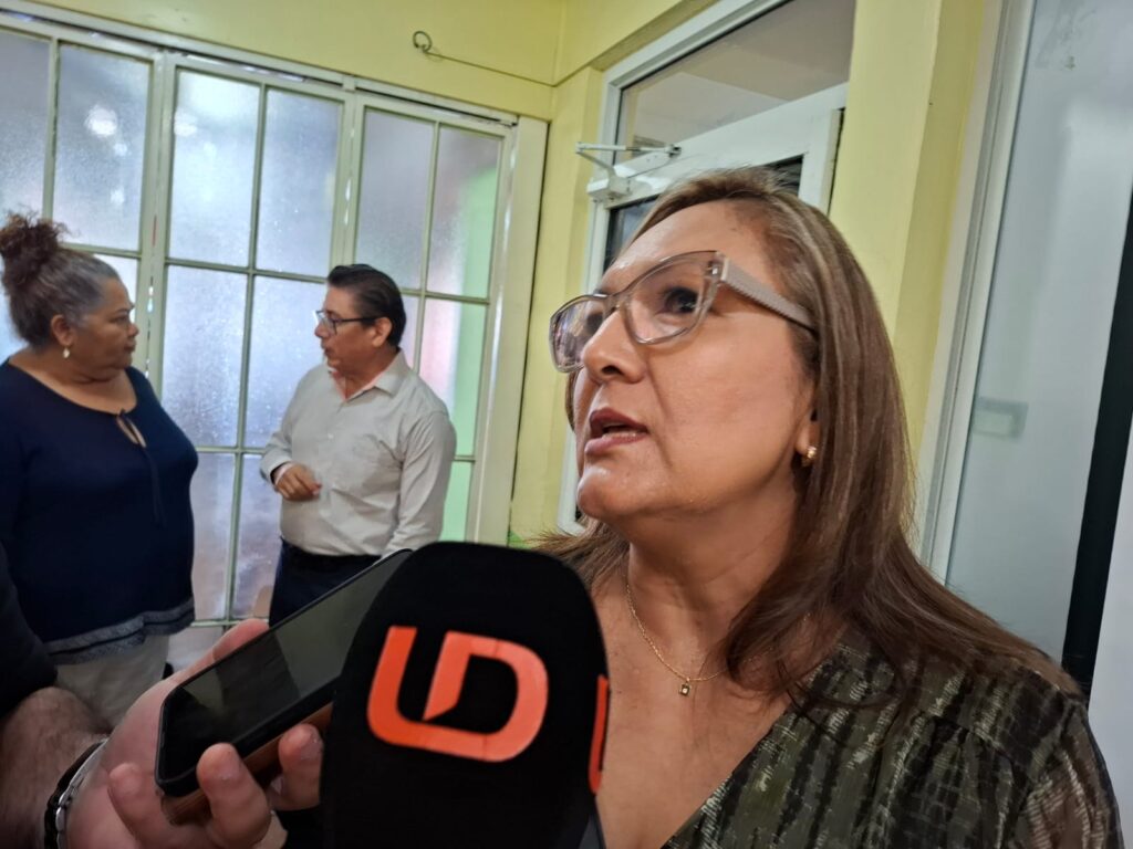 Mujer de perfil hablando hacia un micrófono negro con letras color naranja