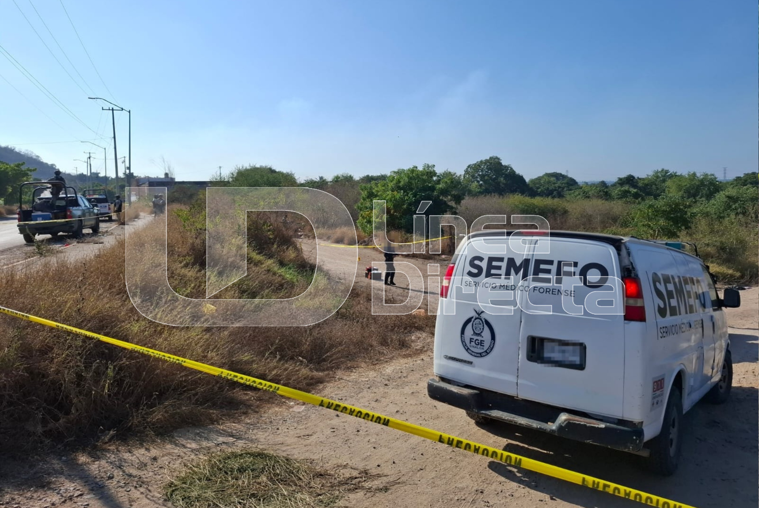 Unidad de la SEMEFO en un costado de una carretera entre matorrales y se observa una cinta amarilla de precaución