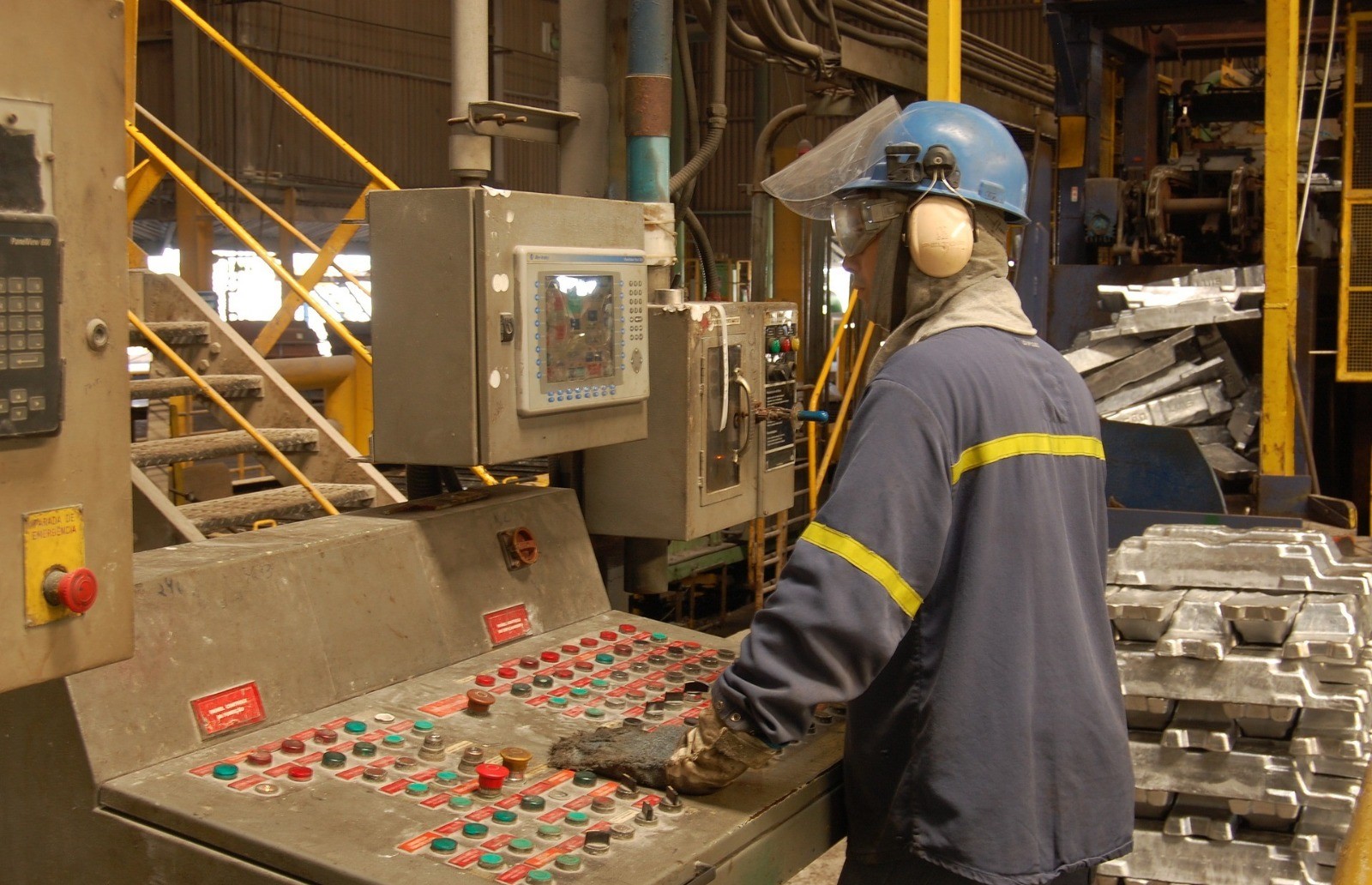 Persona con atuendo de trabajo y casco a lado de una máquina con botones