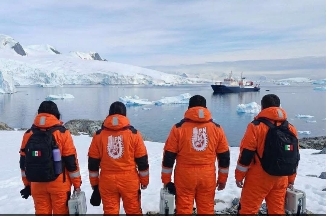 Cuatro personas de espaldas vestidos con un traje naranja en la Antártida