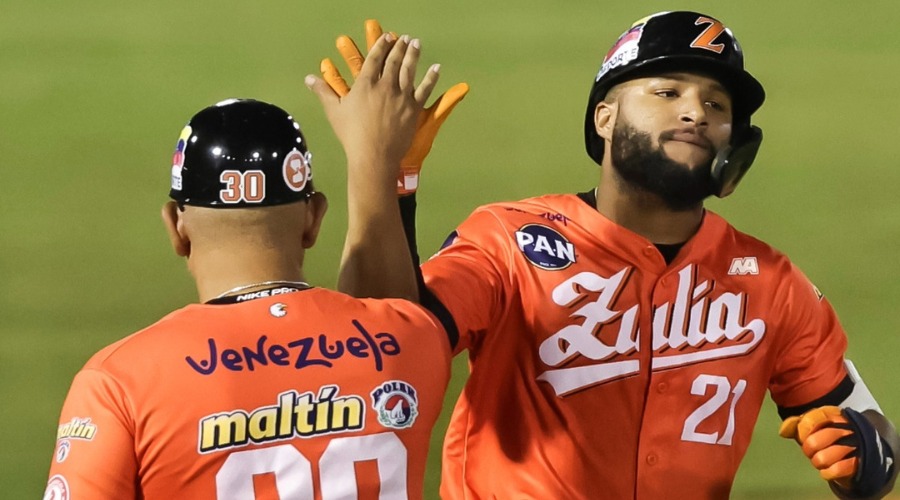 Jugadores de beisbol con uniforme naranja en un estadio chocando sus manos