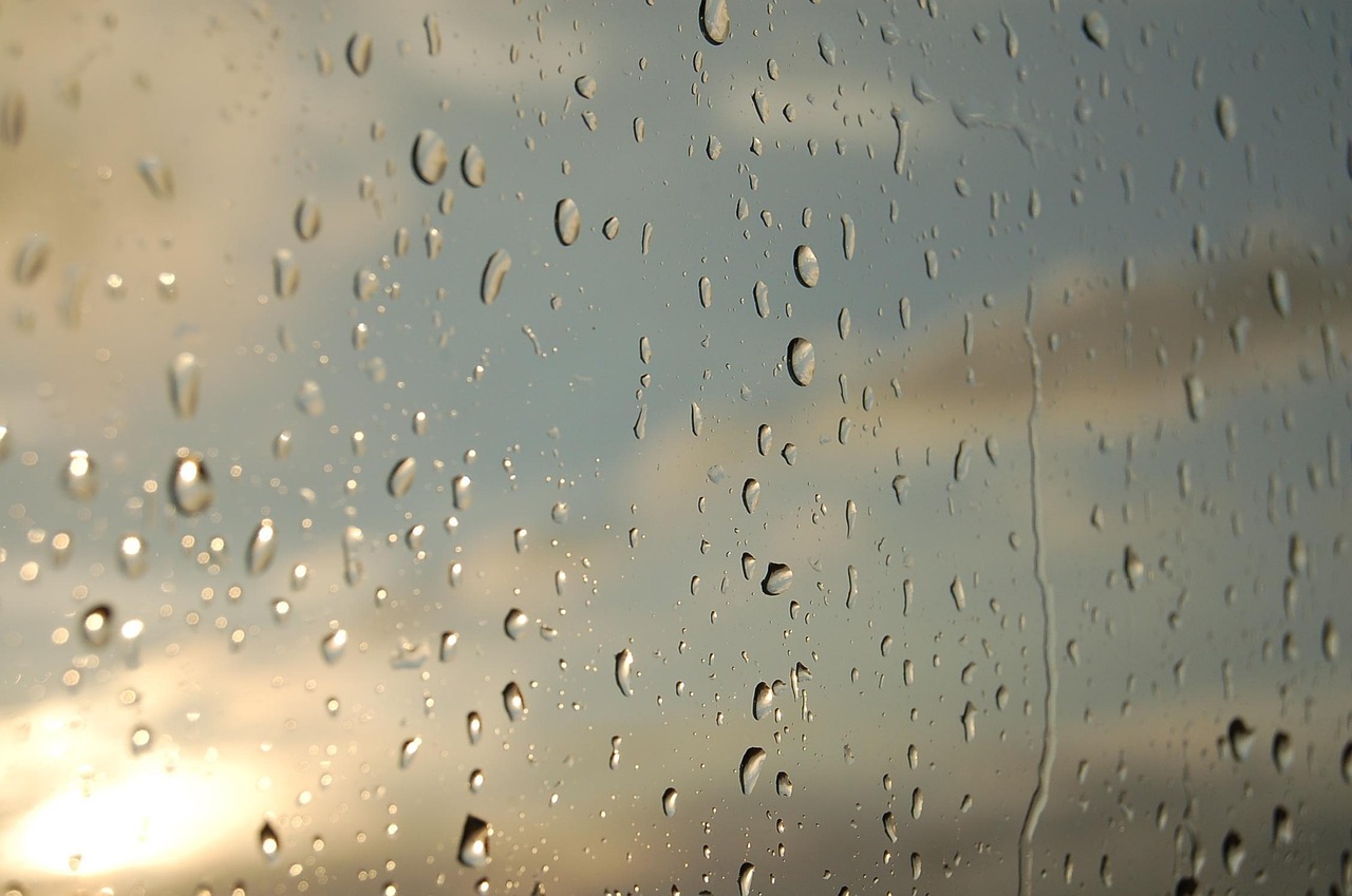 Vidrio con gotas de agua y al fondo un cielo azul con nubes