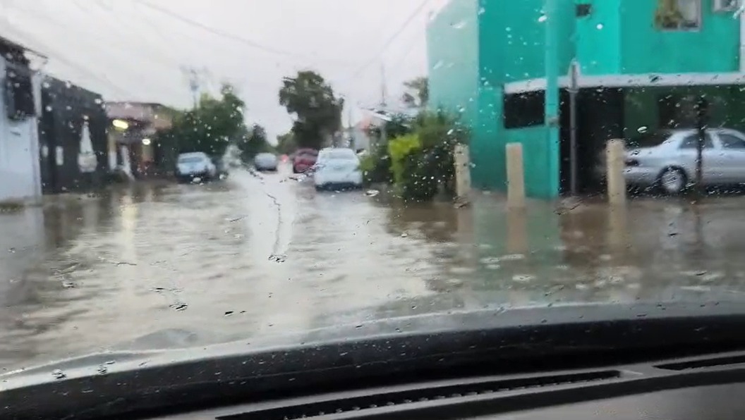 Gotas de agua en el vidrio de un carro, al fondo se observa una calle con grandes charcos de agua